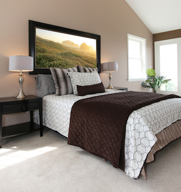 a carpeted room with a high sloping celing, two small bright windows, and a two-person bed with a bedside table and lamp on each side